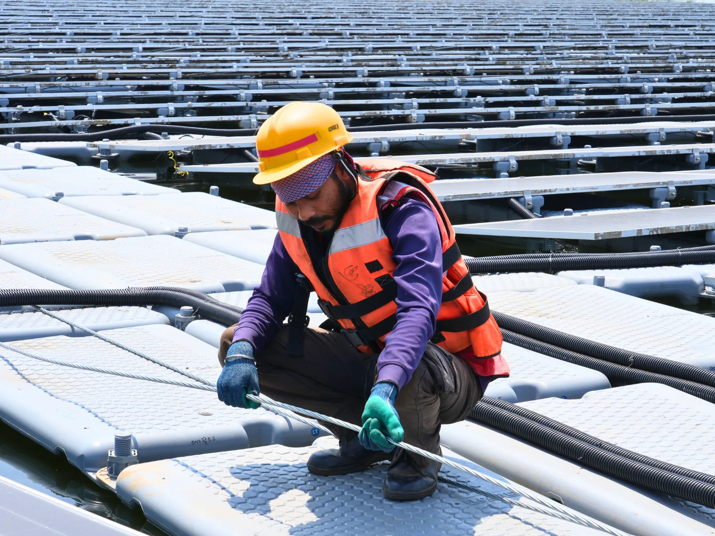 Technician inspecting a mooring cable on a floating solar array during an end-of-life condition assessment