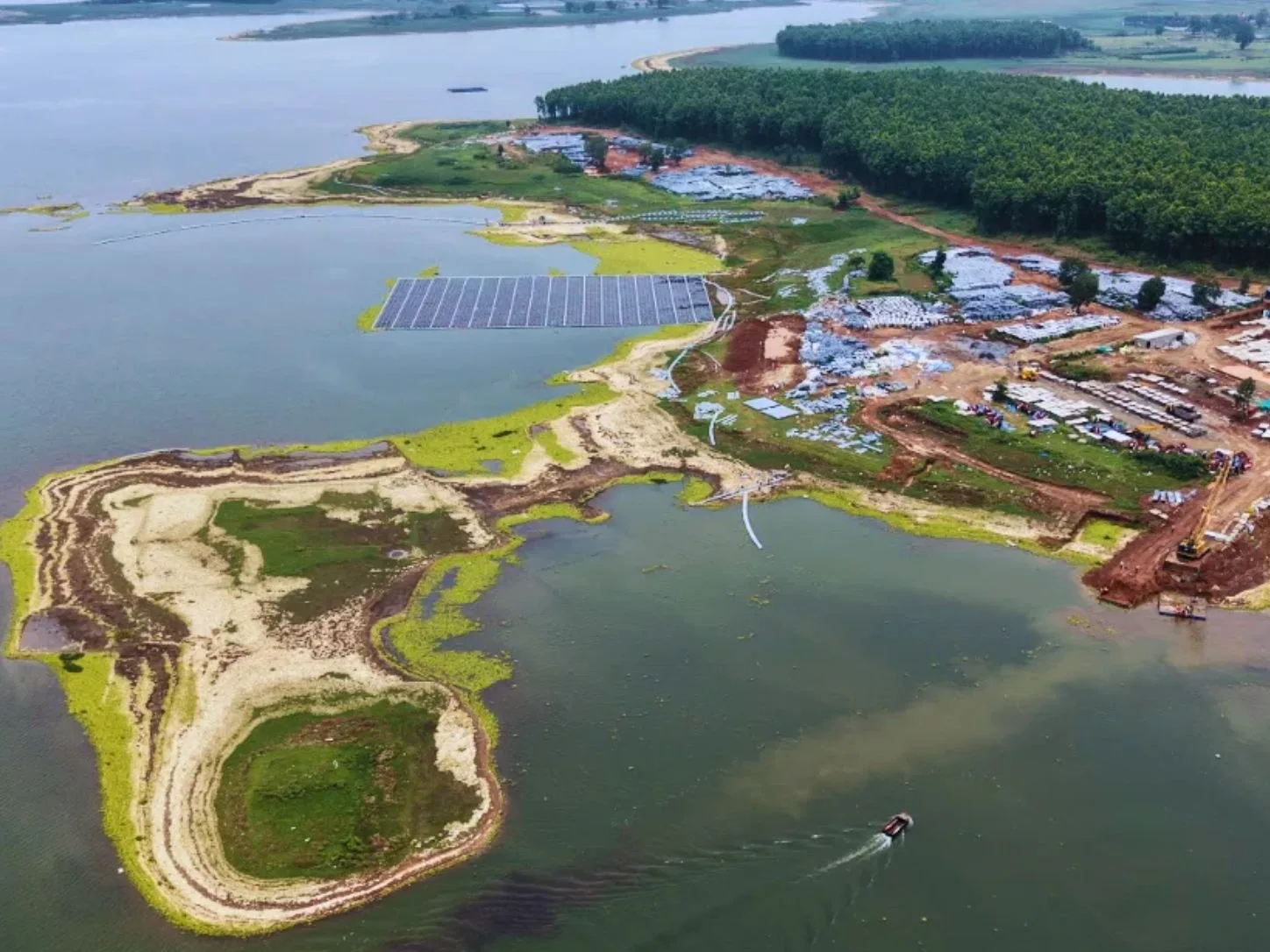 Aerial view of a floating solar array being assembled on a reservoir, with float stockpiles and construction work along the shore