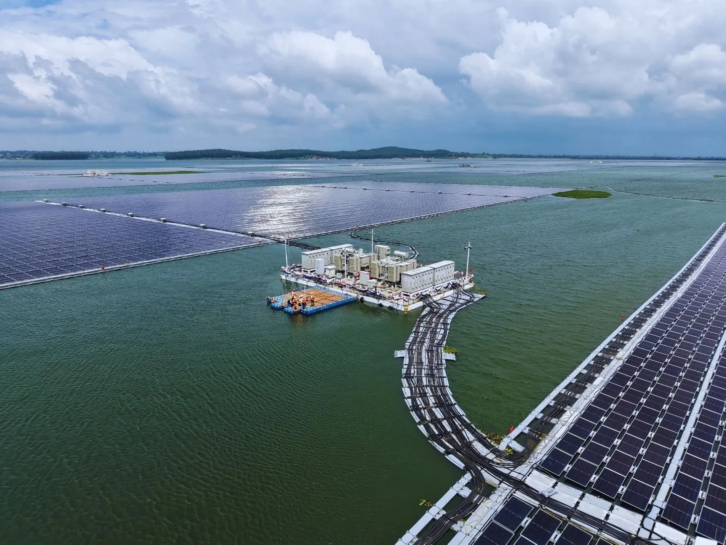 Aerial view of a large floating solar array on an open reservoir with a floating inverter platform and cable routes on the water